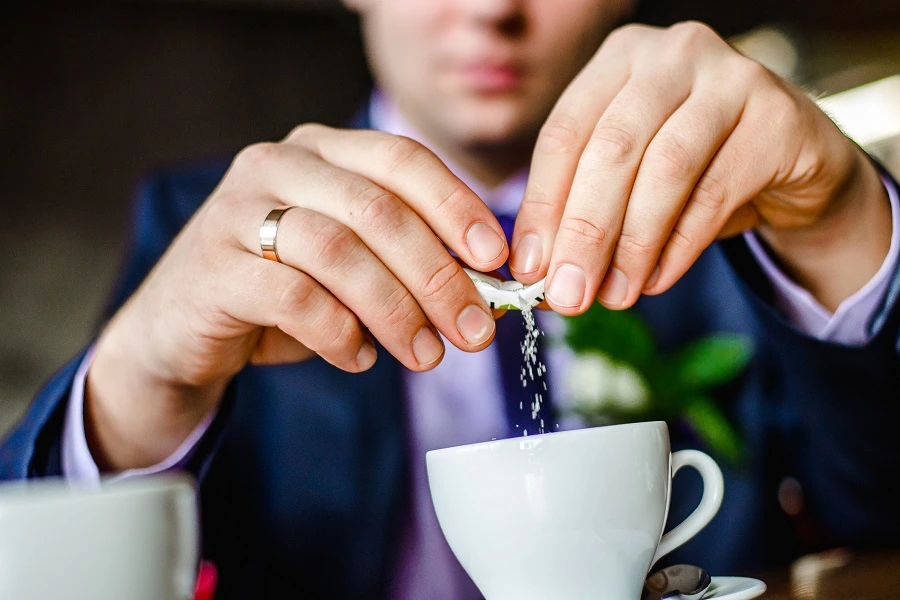man adding sweetener to a drink in a white cup